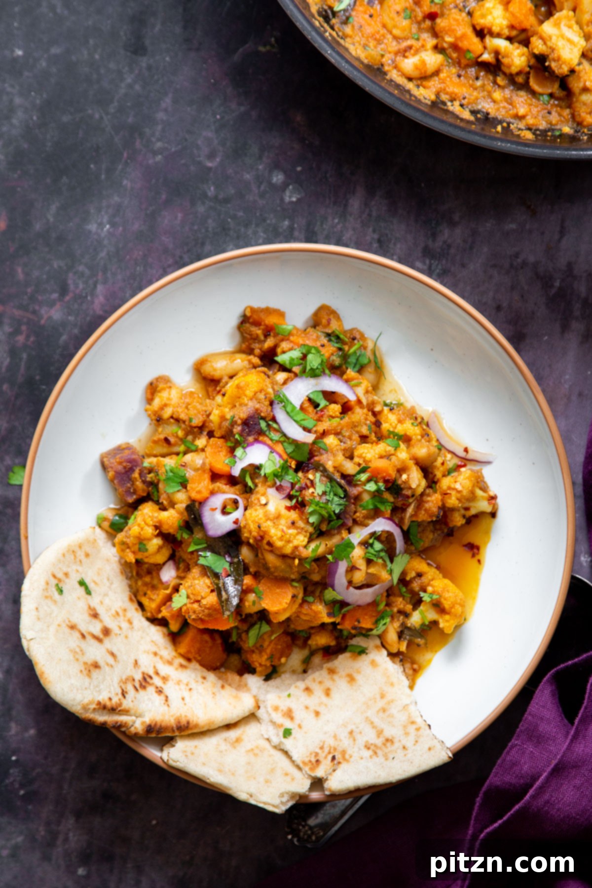 Hearty Vegan Malabar Curry 19 A generous serving of vegan Malabar curry with colorful vegetables and white beans, accompanied by a piece of naan bread.