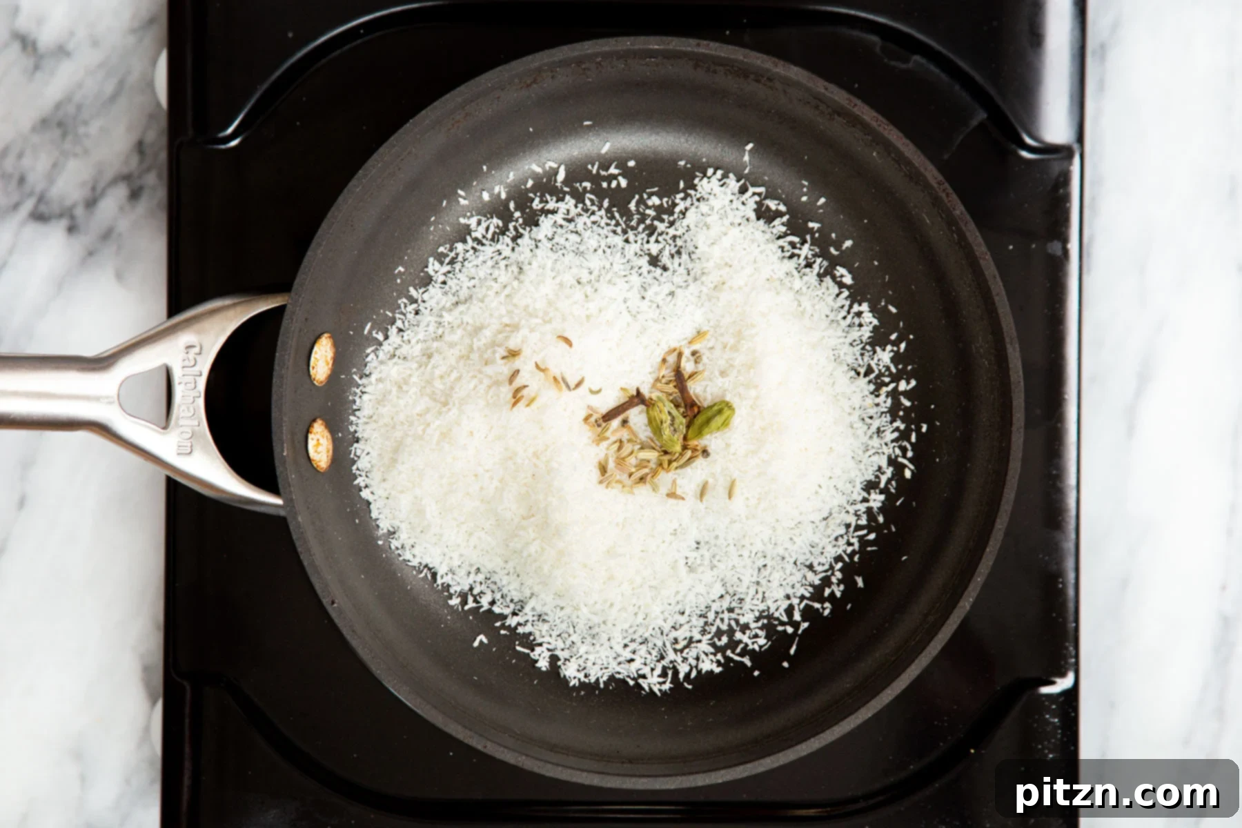Hearty Vegan Malabar Curry 8 Shredded coconut being toasted in a black sautéing pan, turning golden brown.