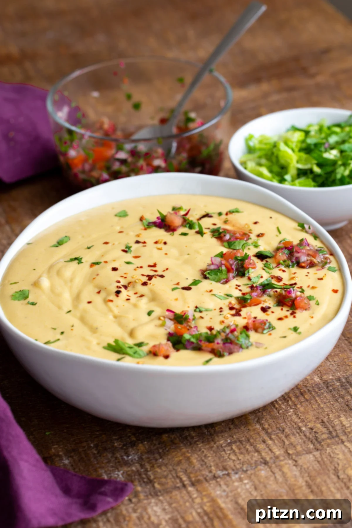 A bowl of vegan cheese sauce topped with vibrant pico de gallo and fresh chopped cilantro.