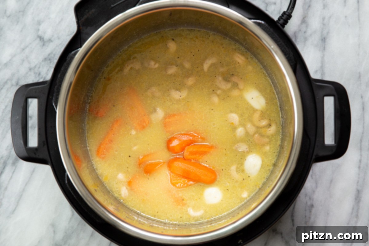 Chopped carrots and raw cashews being carefully added to an Instant Pot with other ingredients for a rich and creamy vegan cheese sauce.