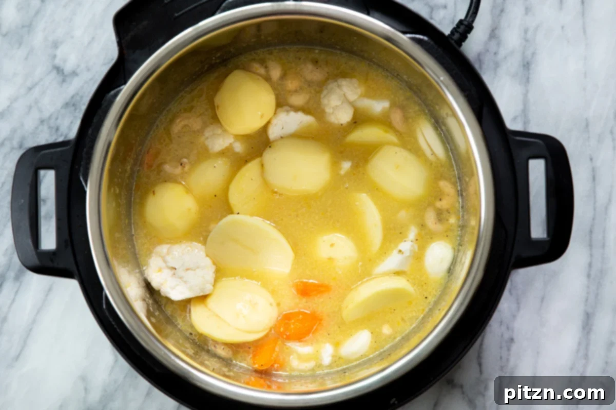 A vibrant mix of potato slices, cauliflower florets, cashews, and carrots being added to an Instant Pot filled with water and spices to create a delicious vegan cheese sauce.