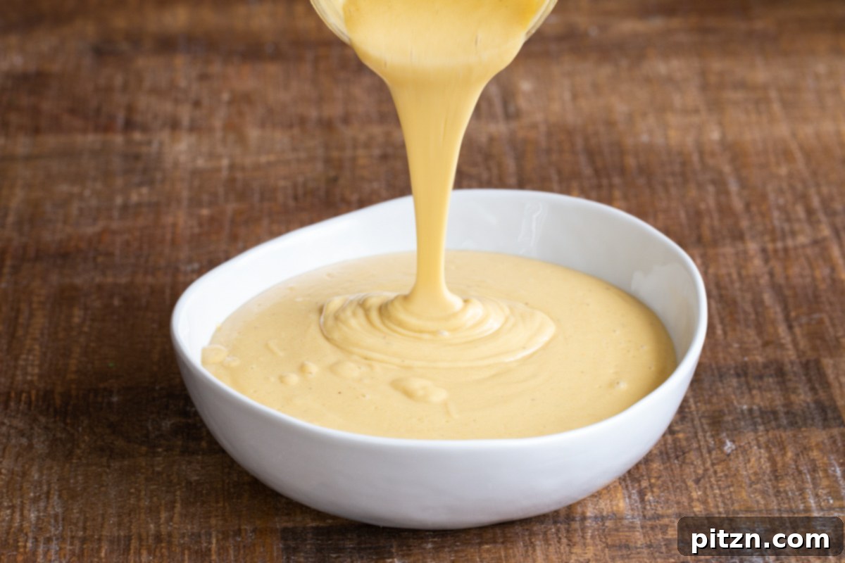 Blended vegan cheese sauce being poured into a small white dish.