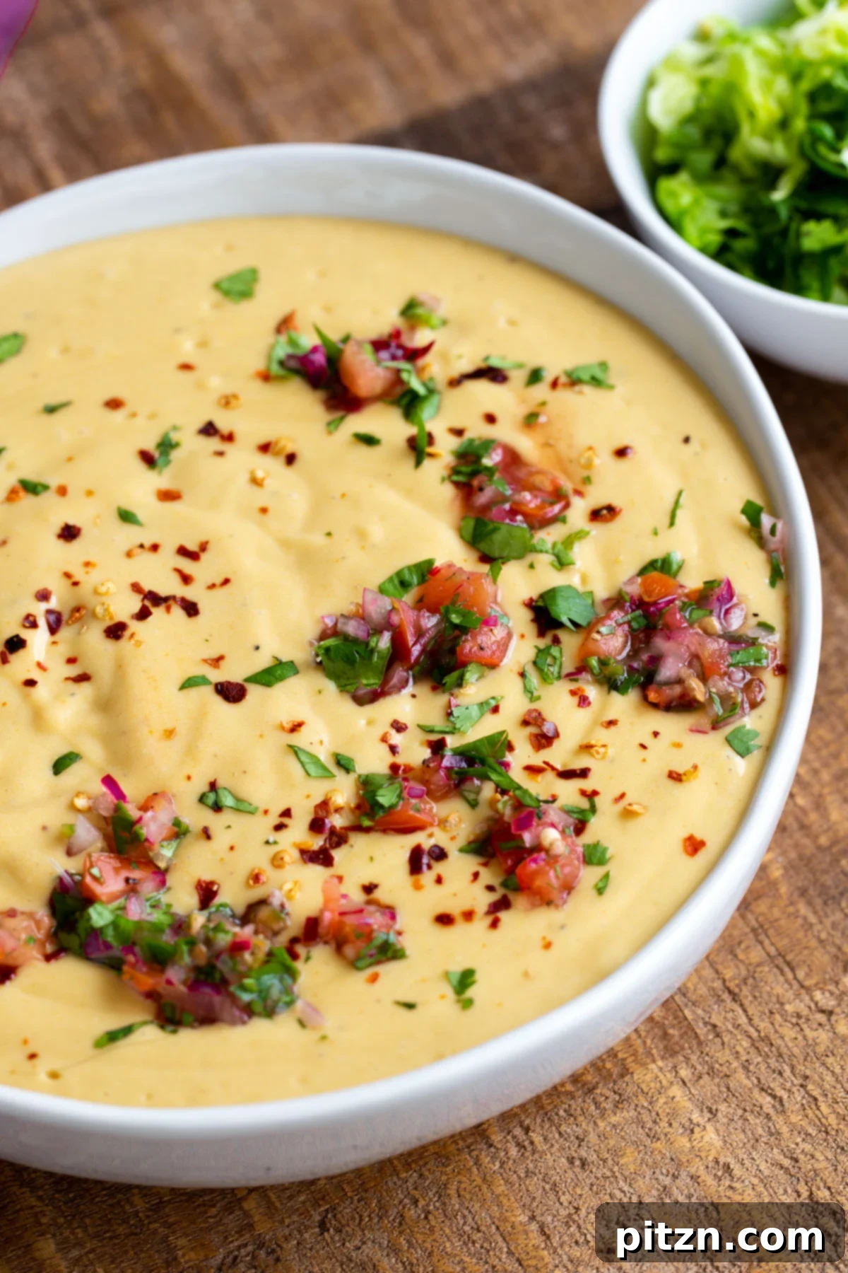 A pristine white bowl filled with Instant Pot Vegan Cheese Sauce, beautifully decorated with fresh chopped herbs and vibrant tomatoes.