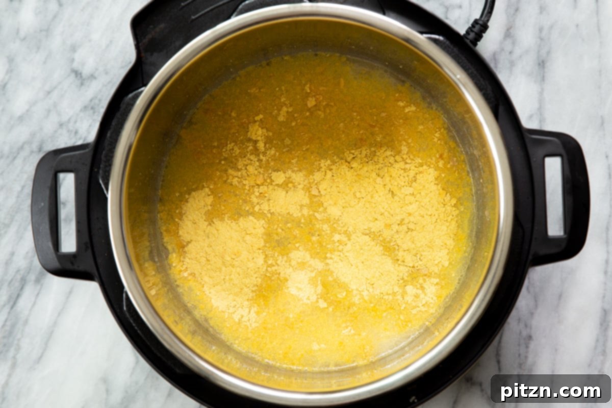Nutritional yeast being added to an Instant Pot containing other ingredients for vegan cheese sauce, showcasing the layering process.