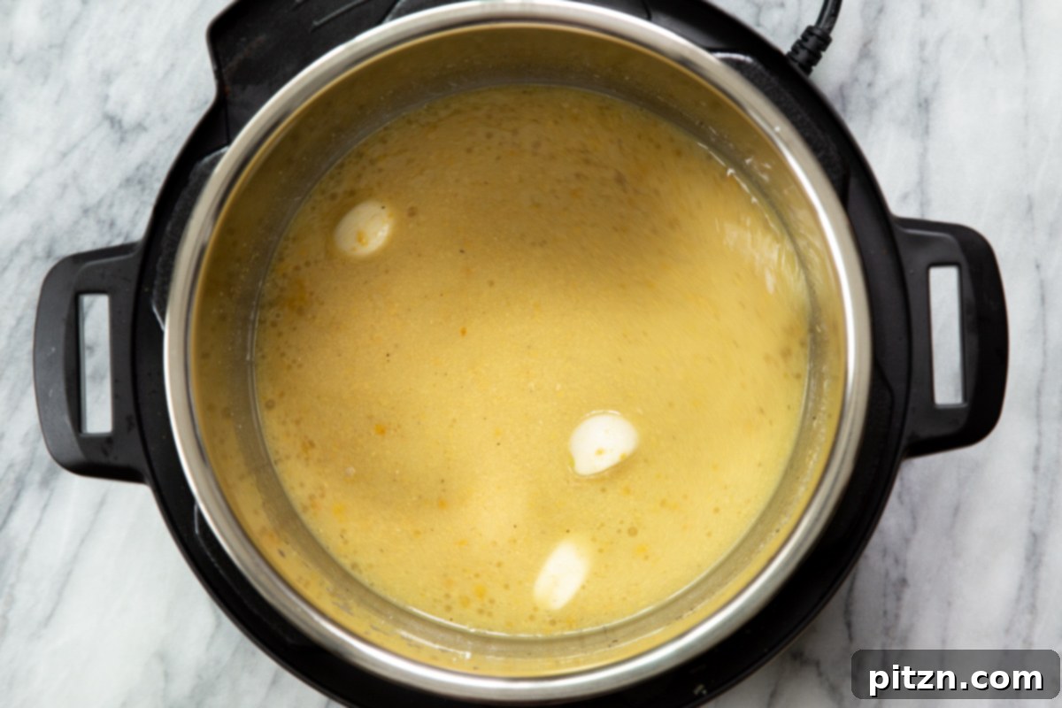 Fresh garlic cloves being added to the Instant Pot along with other vegan cheese sauce ingredients, contributing to its savory depth.