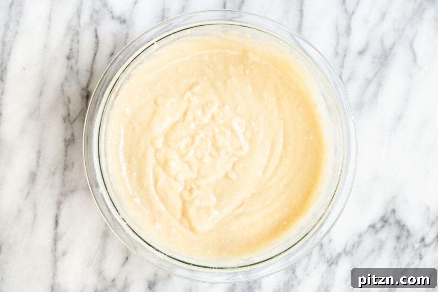 Smooth vegan cake batter resting in a clear glass bowl, ready for the next stage of baking.