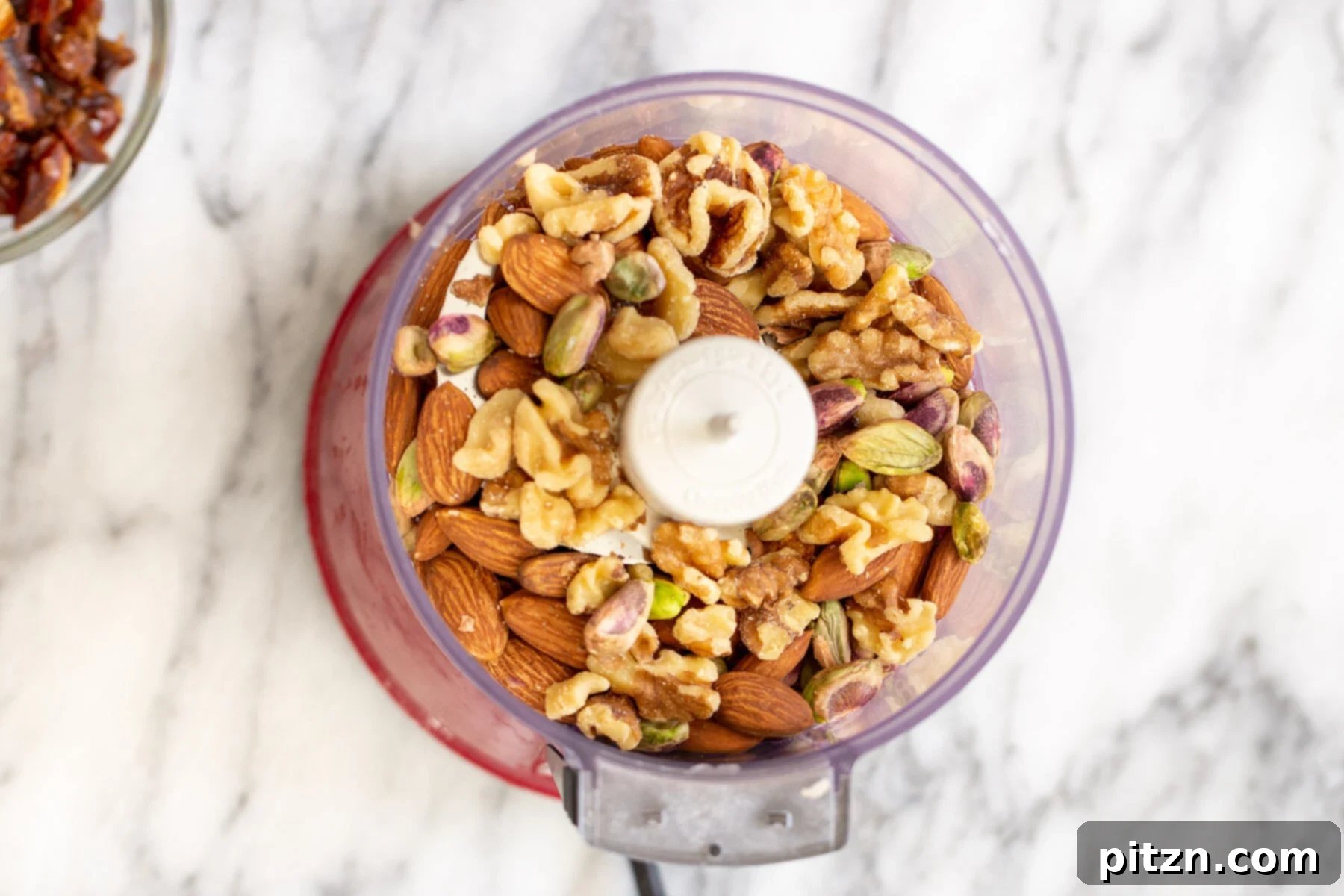 A mix of raw almonds, walnuts, and pistachios awaiting their transformation in a food processor container.