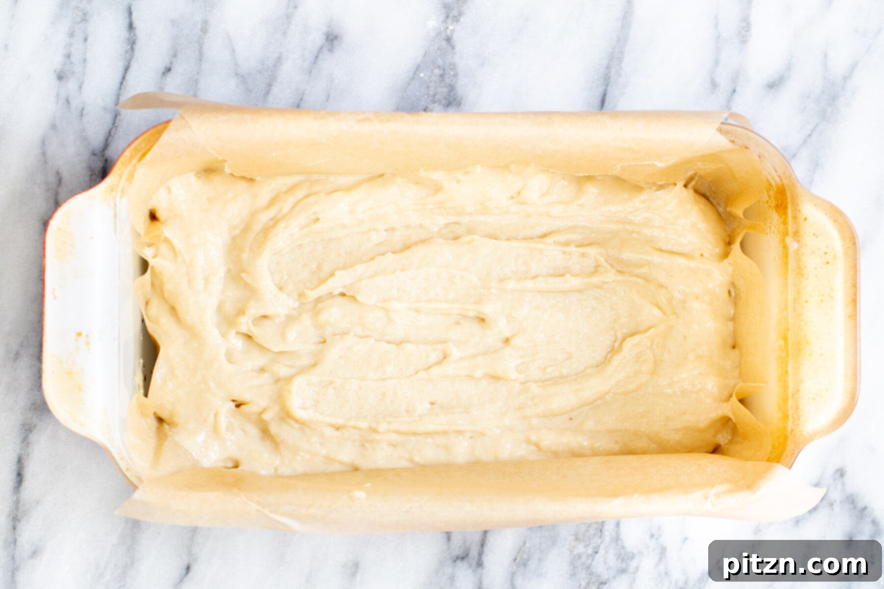 Smooth vegan cake batter being carefully spread into a loaf pan, creating an even base layer.