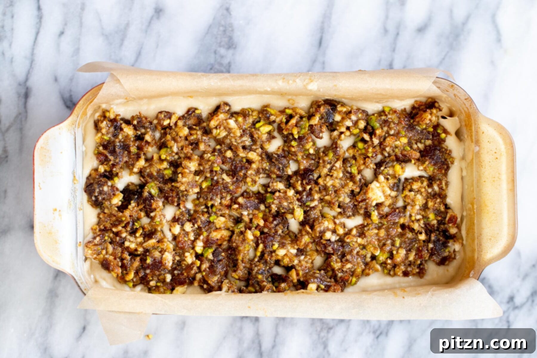 The final layer of baklava topping being spread over the cake batter in the loaf pan, ready for baking.