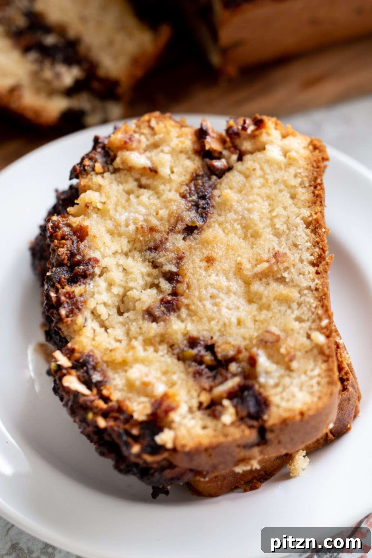 A perfectly sliced piece of vegan baklava cake resting on a white cake plate, highlighting the beautiful nut swirl.