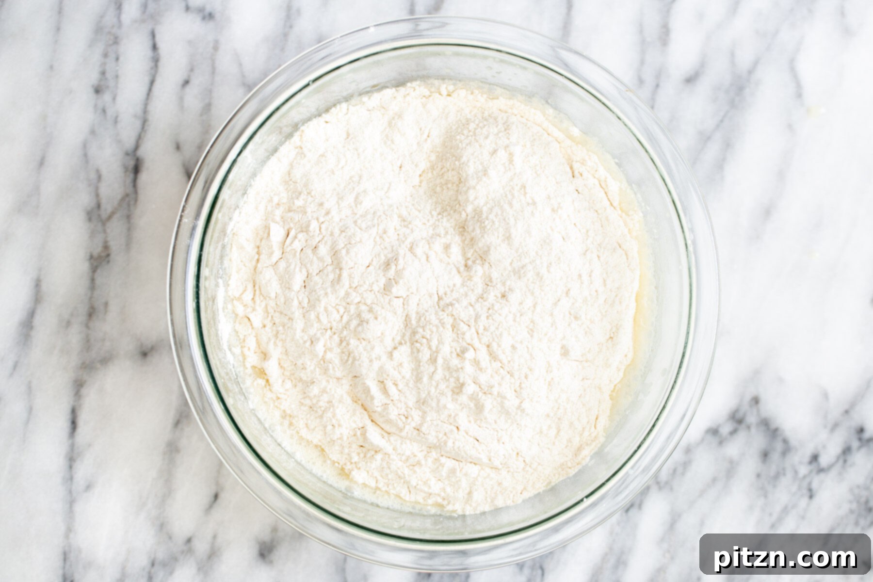 Dry cake mix patiently waiting in a large glass mixing bowl, poised to join the wet ingredients.