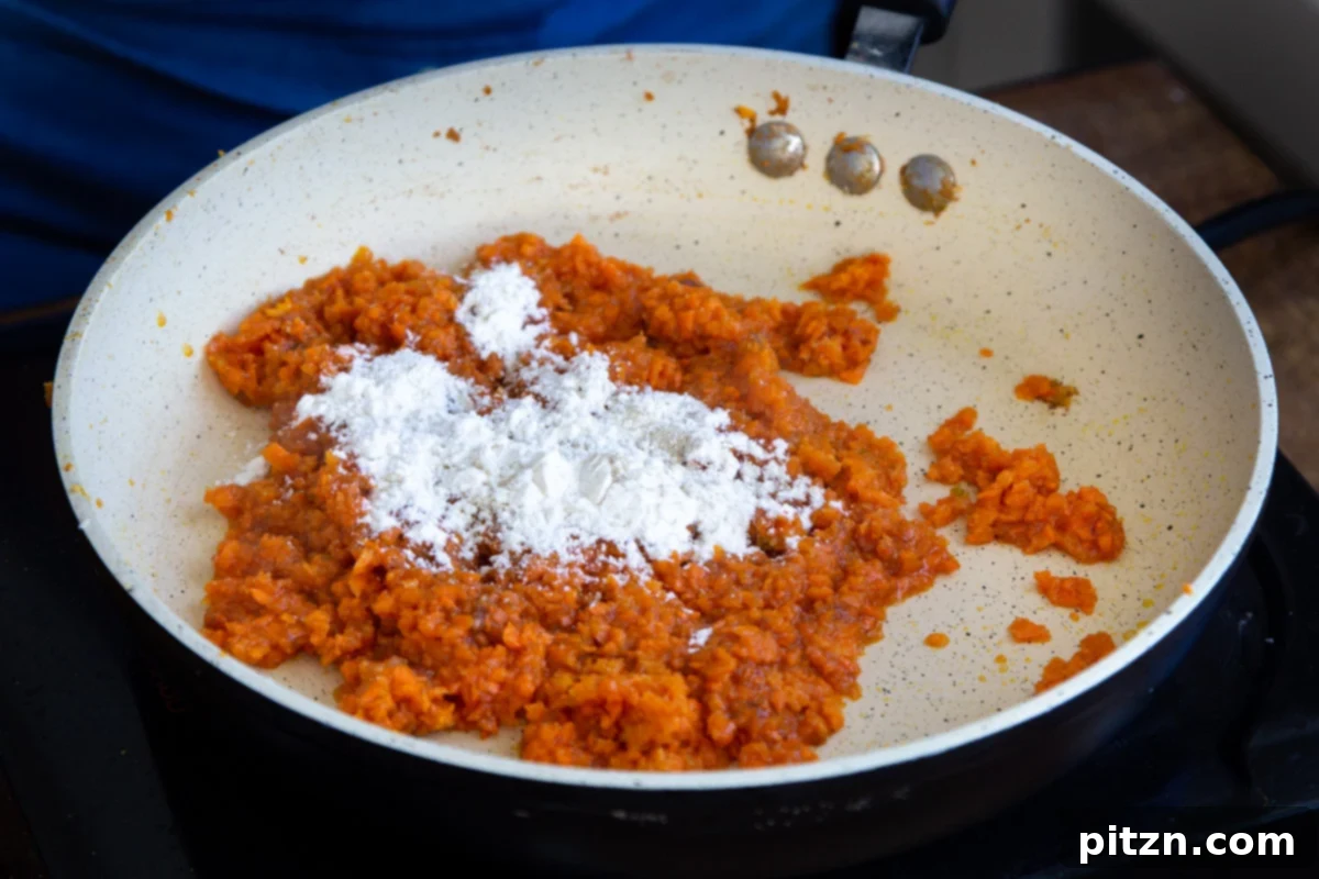 Layered Vegan Carrot Halwa Coconut Burfi 16 flour being added to shredded carrots in a frying pan