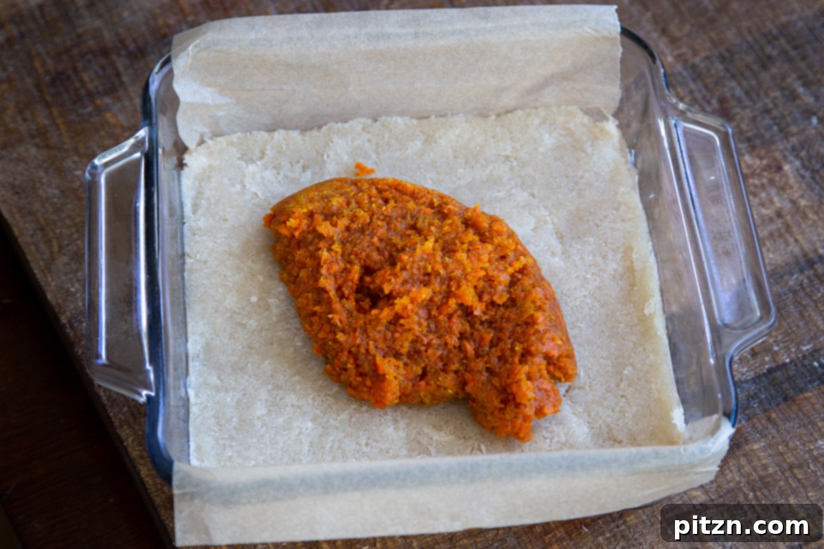 Layered Vegan Carrot Halwa Coconut Burfi 18 carrot halwa layer being spread over coconut burfi layer in a square glass pan