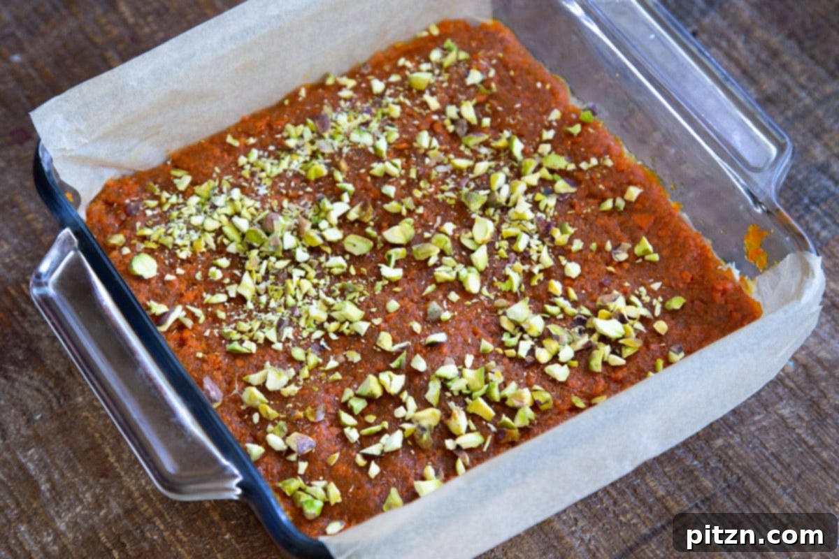 Layered Vegan Carrot Halwa Coconut Burfi 20 carrot halwa coconut burfi bars topped with chopped pistachios in a glass dish