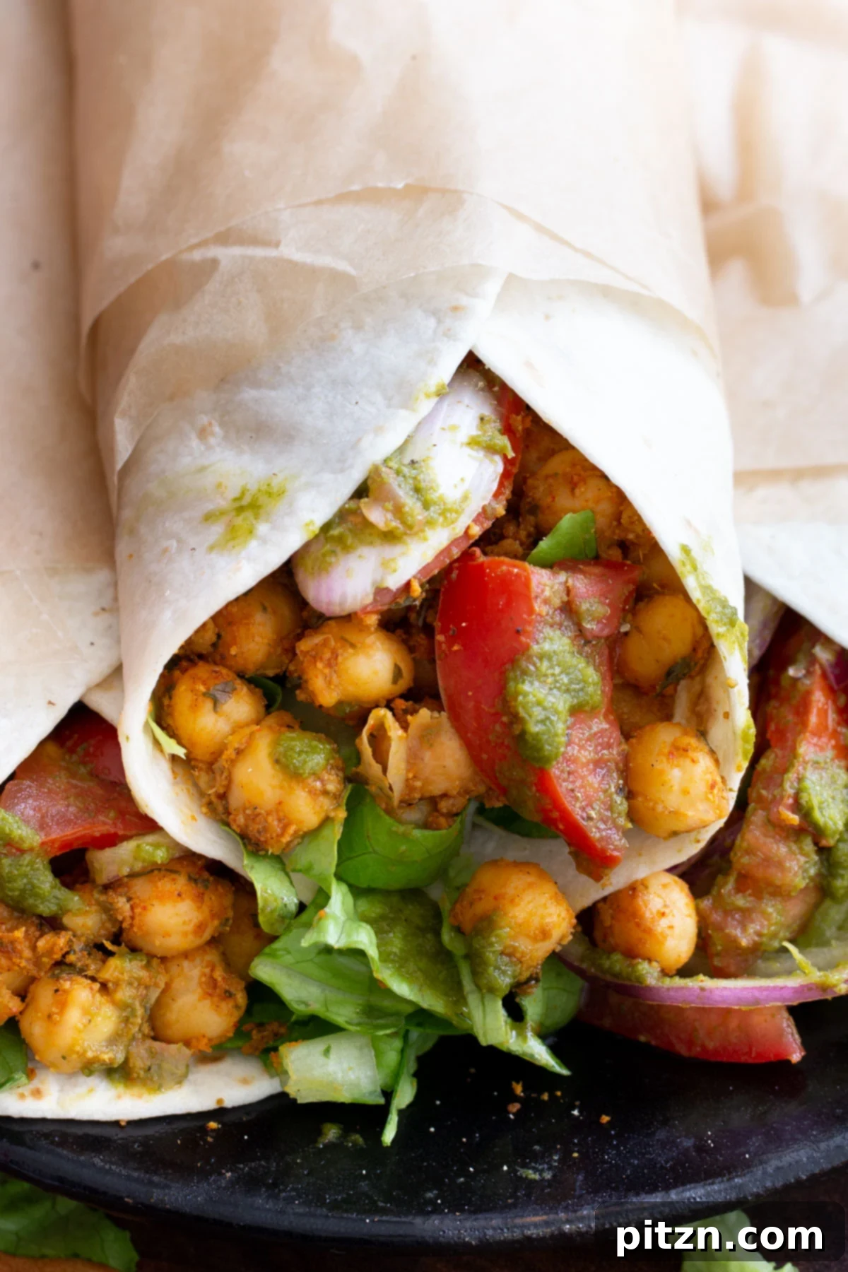 Tangy Chickpea Wraps 2 Close-up of three vibrant Chickpea Kathi Rolls, garnished with fresh cilantro, sliced tomatoes, and red onions, served with a side of green chutney.