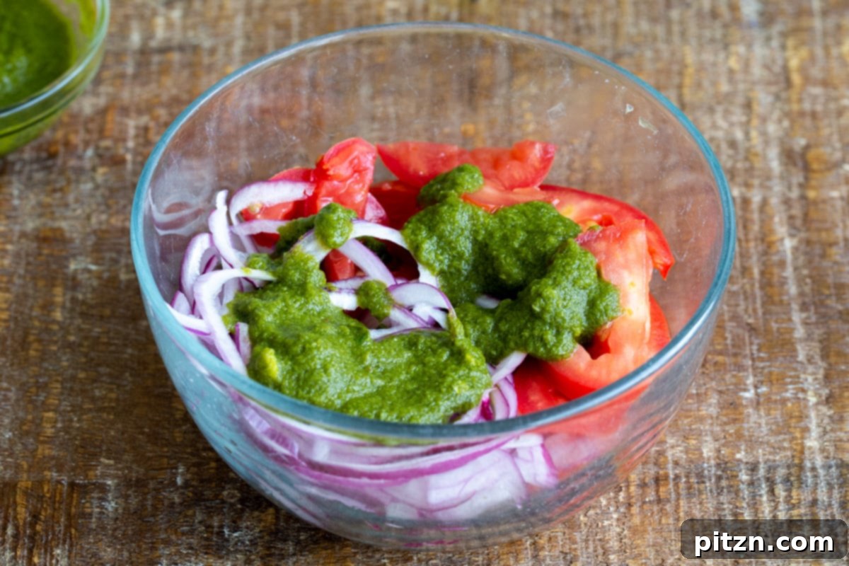 Tangy Chickpea Wraps 8 Thinly sliced red onions, tomatoes, and a generous dollop of fresh green mint chutney, ready to be mixed in a clear glass bowl.
