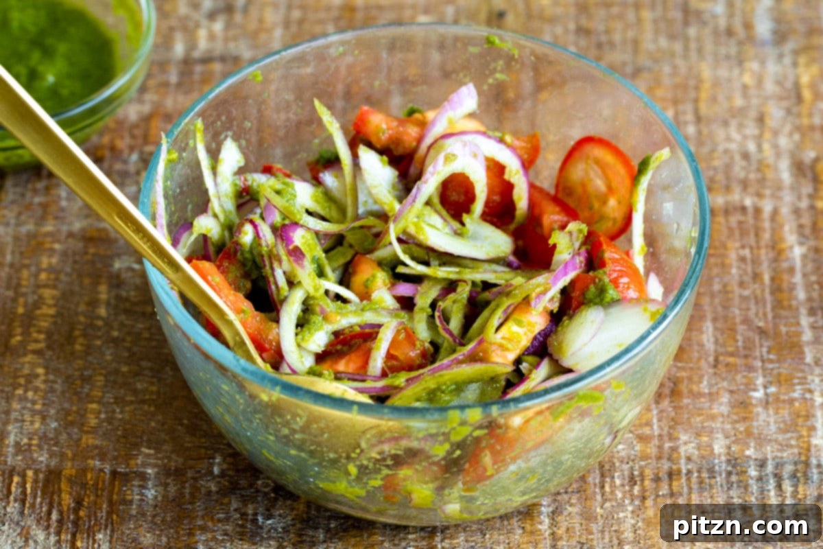 Tangy Chickpea Wraps 9 Hand mixing sliced red onions, tomatoes, and vibrant cilantro mint chutney in a glass bowl to create the fresh Kathi Roll topping.