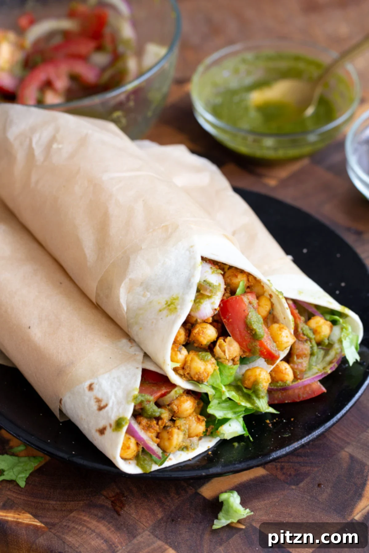 Tangy Chickpea Wraps 13 Three beautifully presented chickpea Kathi rolls on a black plate, two wrapped and one open, showcasing the rich filling. Labeled as nut-free and soy-free.