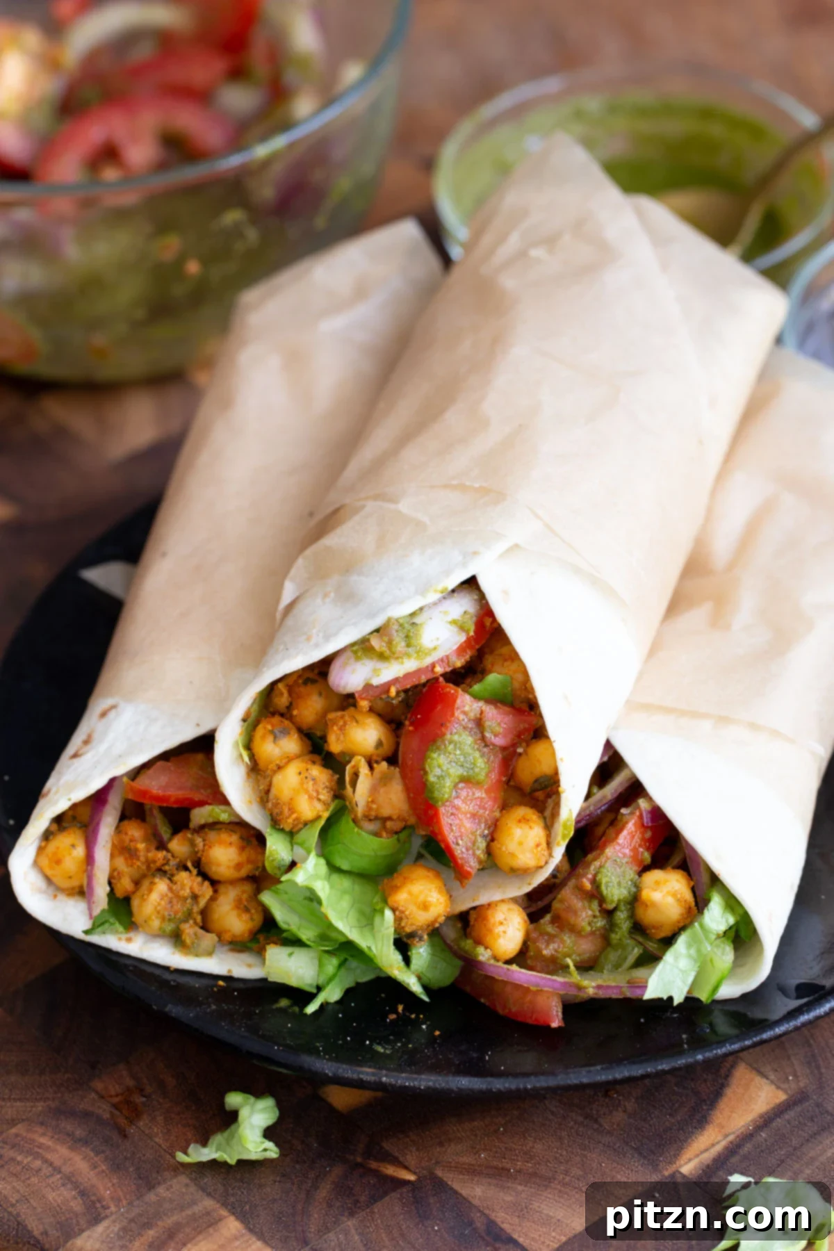 Tangy Chickpea Wraps 3 Three perfectly rolled Chana Kathi Rolls arranged on a dark plate, showcasing their inviting golden wraps and hints of fresh filling.