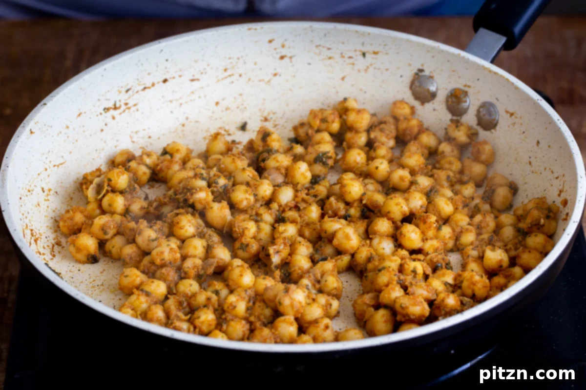 Tangy Chickpea Wraps 7 Close-up of warmly spiced chickpeas simmering in a pan, absorbing the rich flavors of the Indian spices.