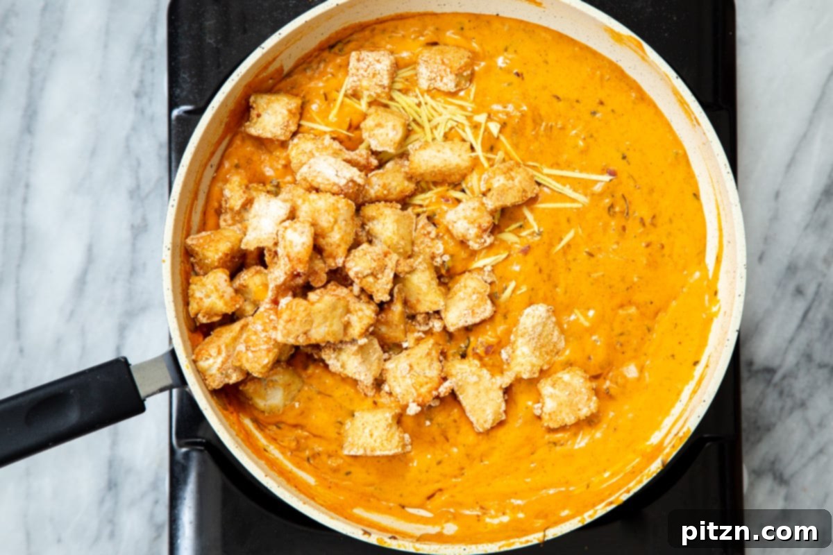 Flavorful Lasooni Vegan Chicken Curry, Entirely Tomato-Free 14 Crispy baked tofu chunks being gently added to the simmering red bell pepper sauce in a pan.