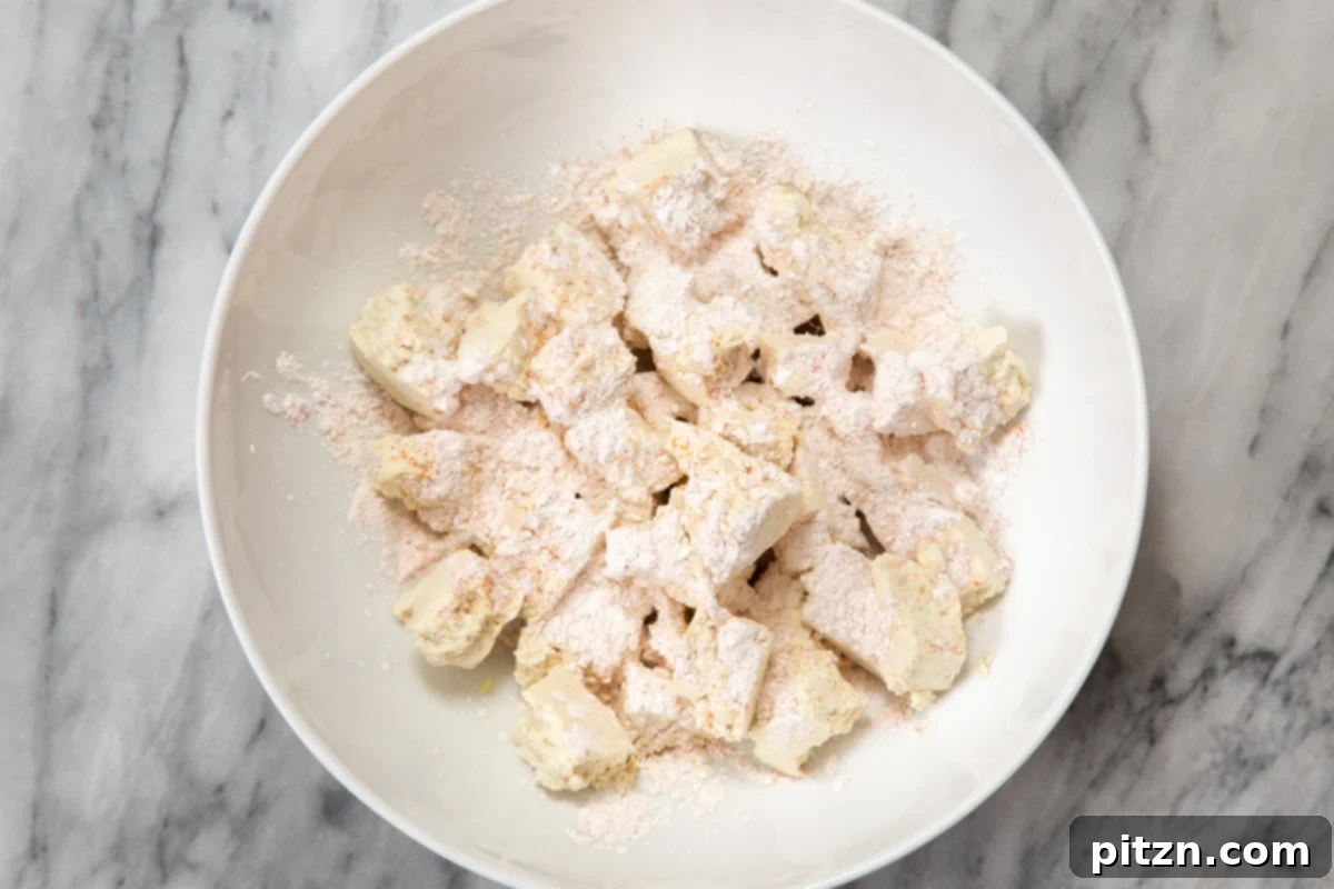 Flavorful Lasooni Vegan Chicken Curry, Entirely Tomato-Free 7 Torn tofu pieces in a white bowl, generously coated with a spiced cornstarch mixture, ready for baking.
