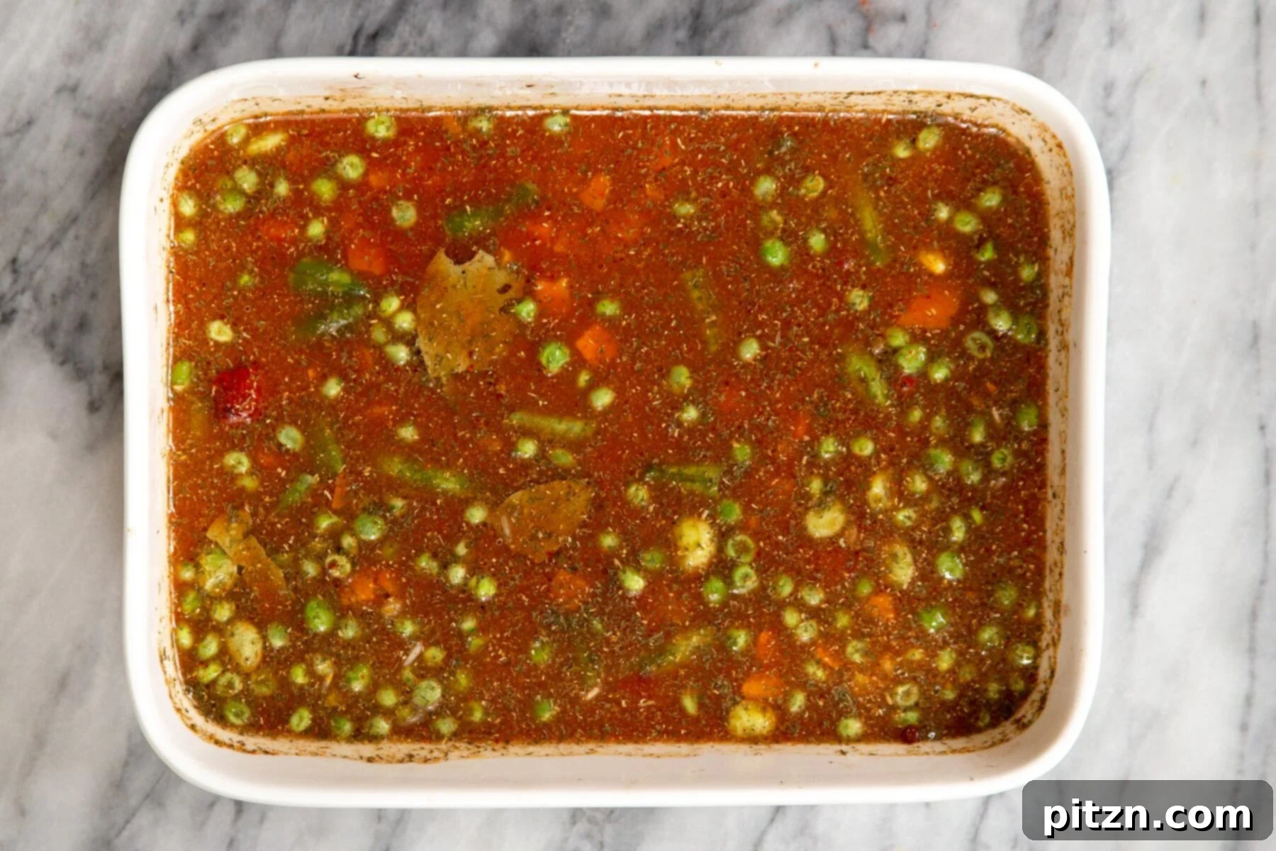 A white casserole dish filled with all the ingredients for baked rice, perfectly mixed and smoothed, ready to go into the oven.