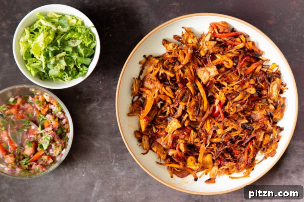 Quick & Easy Vegan Jackfruit Tacos 16 baked jackfruit taco meat in a white bowl next to two small bowls with chopped lettuce and salsa