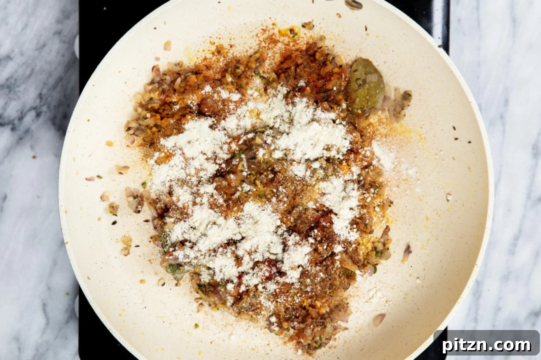 Vegan Tofu Matar 17 flour being added to a sauteeing pan with ginger and onion