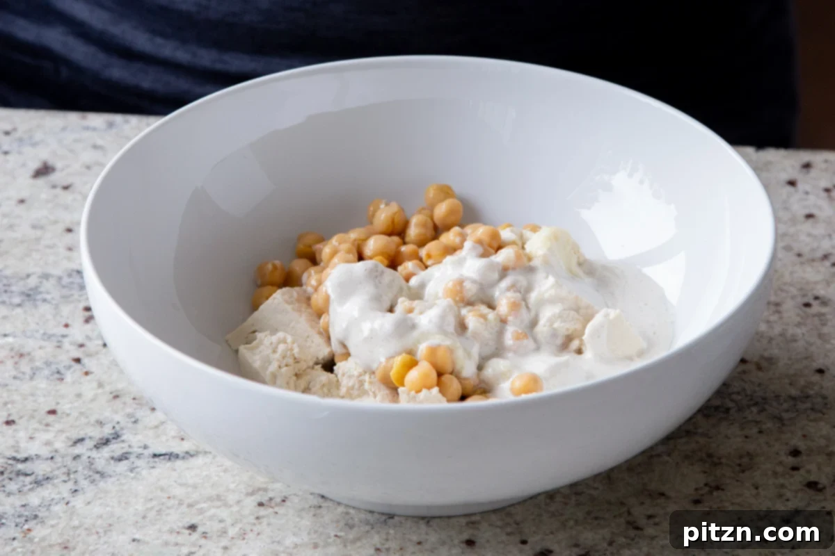 Creamy Fenugreek Tofu and Chickpea Curry 7 Torn tofu and chickpeas in a bowl with non-dairy cream added for marination