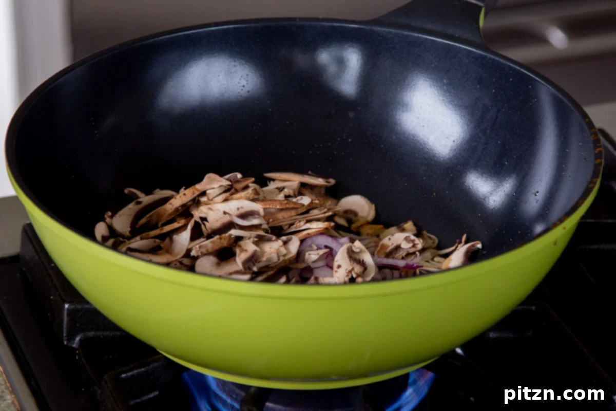 Decadent Vegan Butter Chicken Ramen 12 Freshly sliced mushrooms and onions added to a hot wok, ready to be sautéed.