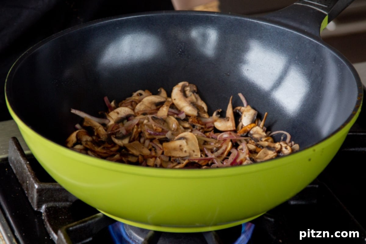 Decadent Vegan Butter Chicken Ramen 13 Sautéed mushrooms and onions in a wok, perfectly cooked and softened.