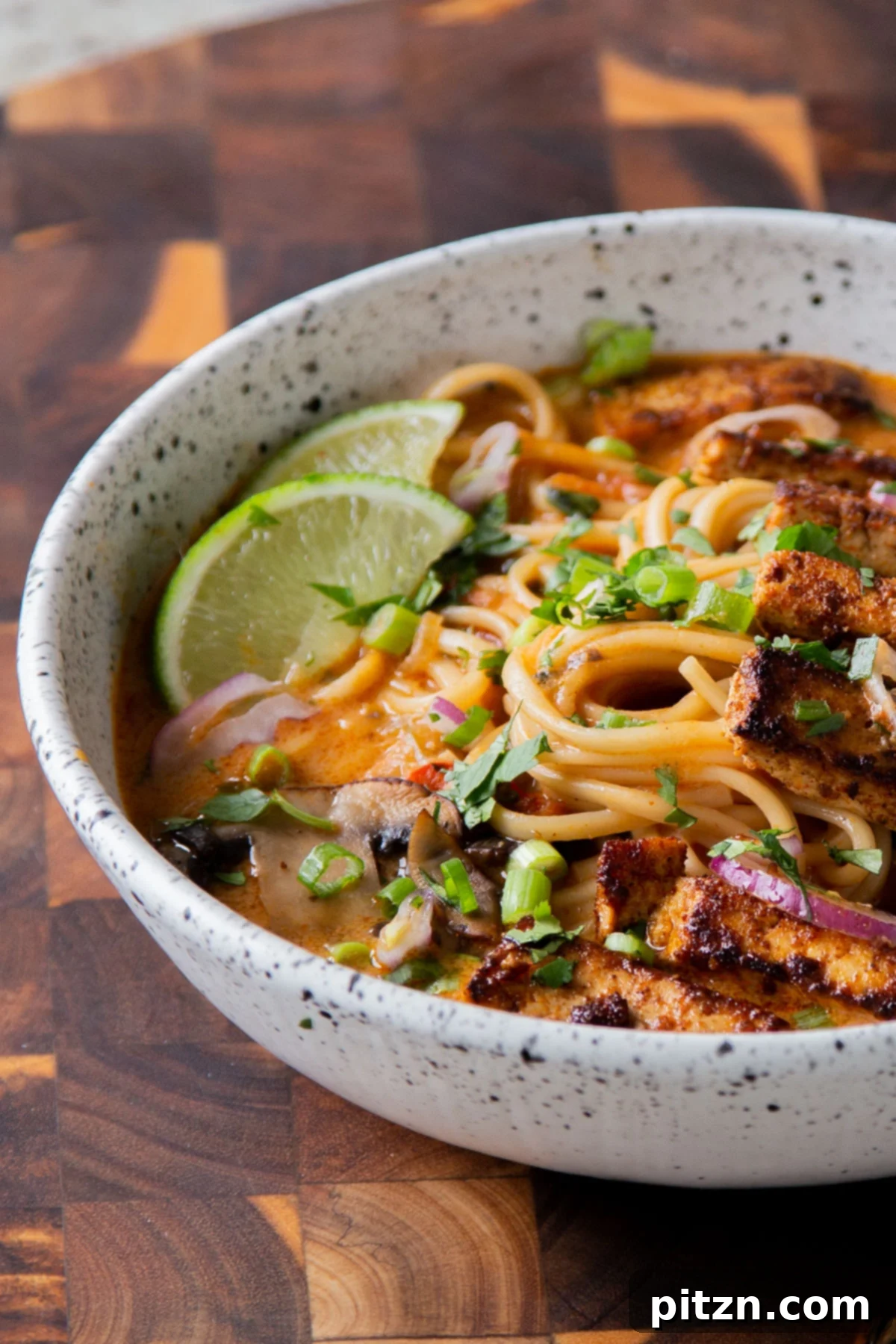 Decadent Vegan Butter Chicken Ramen 5 Close-up view of a bowl of Vegan Butter Chicken Ramen, showcasing the crispy tofu and lime wedge garnish