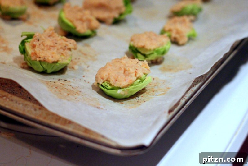 Halved Brussels sprouts coated in a breading mixture, ready to be baked on a parchment-lined tray