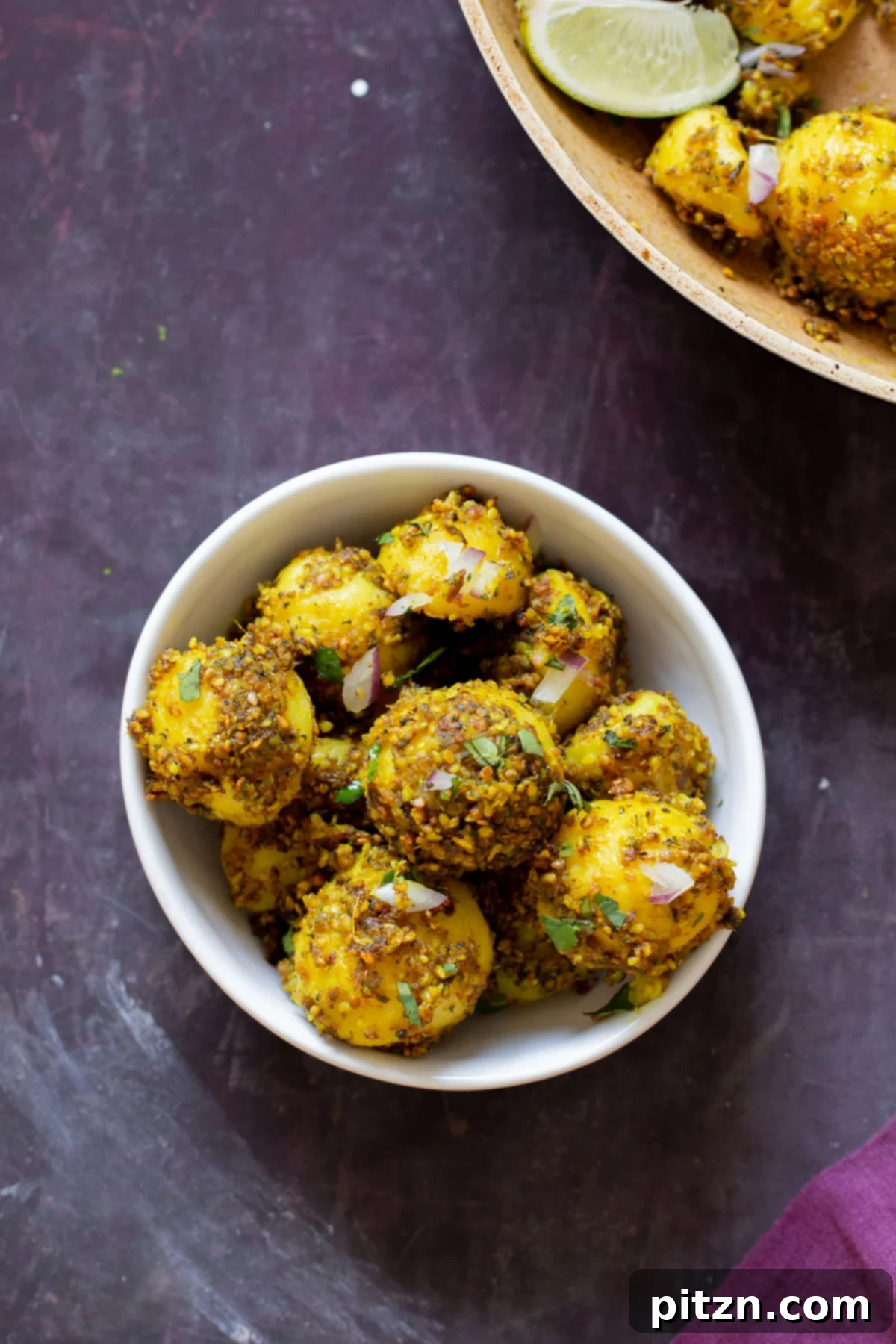 Perfectly roasted peanut sesame potatoes in a rustic serving bowl, with a hot frying pan in the background.