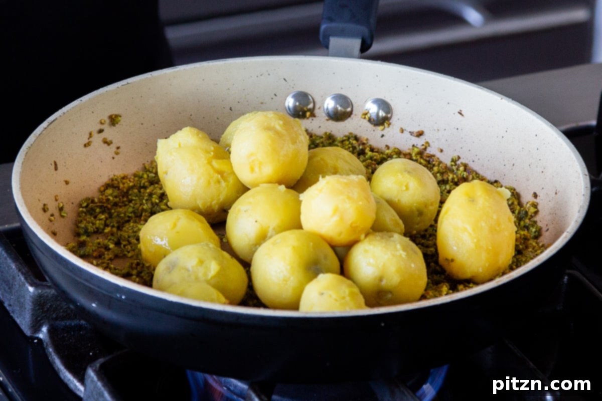 Adding tender, cooked and peeled potatoes to the pan with the sizzling peanut-sesame spice mixture.