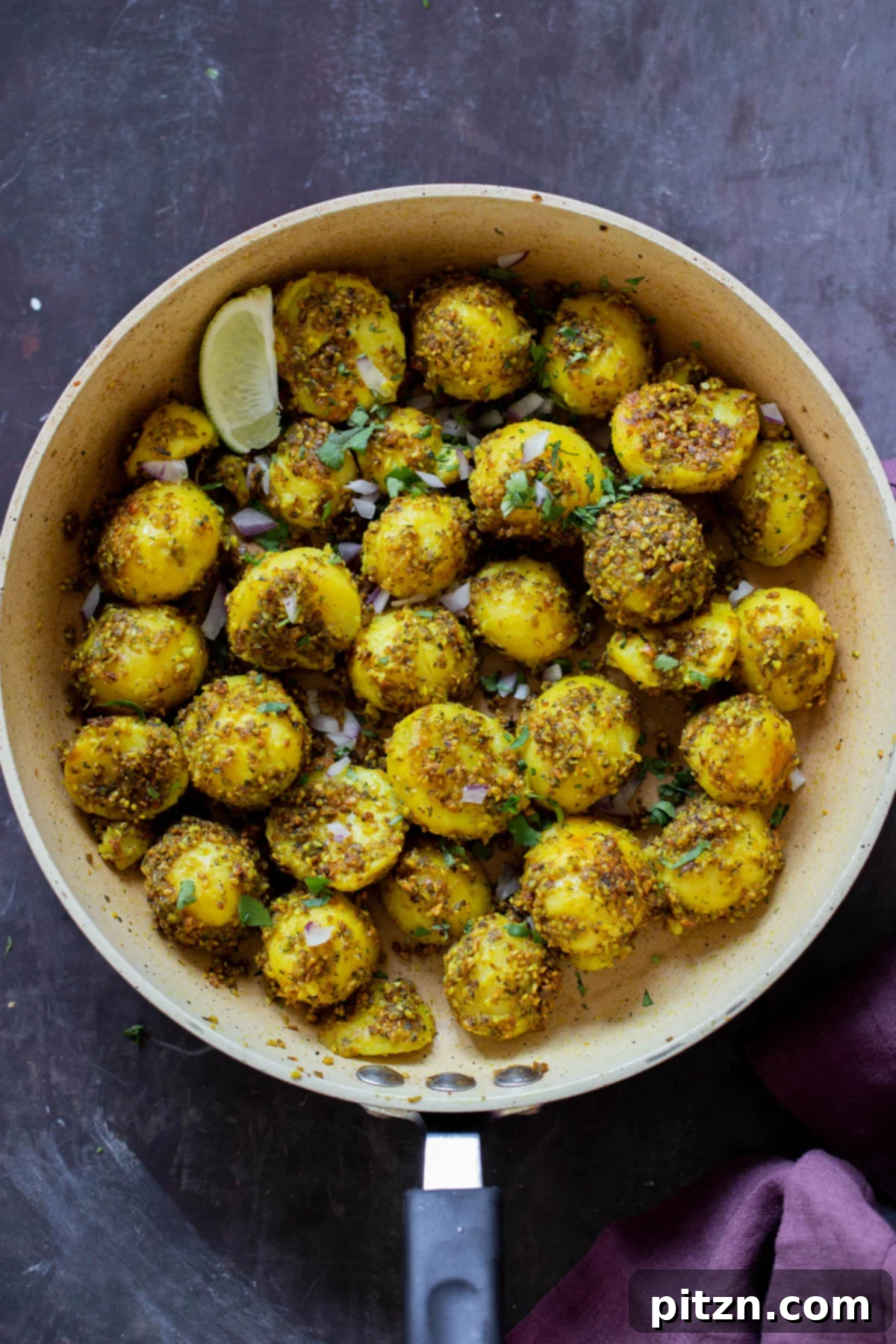 Close-up of golden peanut sesame potatoes sizzling in a frying pan after cooking, garnished with fresh herbs.