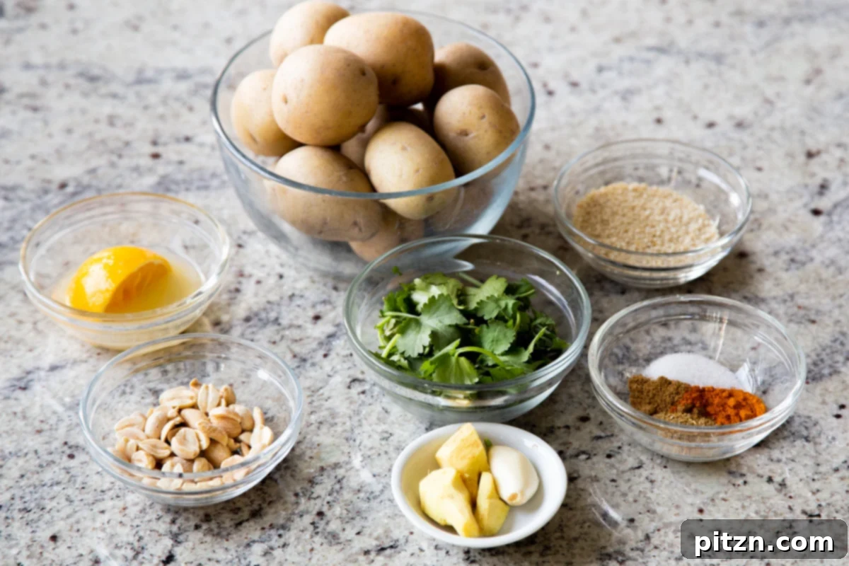 Various ingredients for the recipe, including whole potatoes, peanuts, sesame seeds, and bowls of ground spices, laid out on a kitchen counter.
