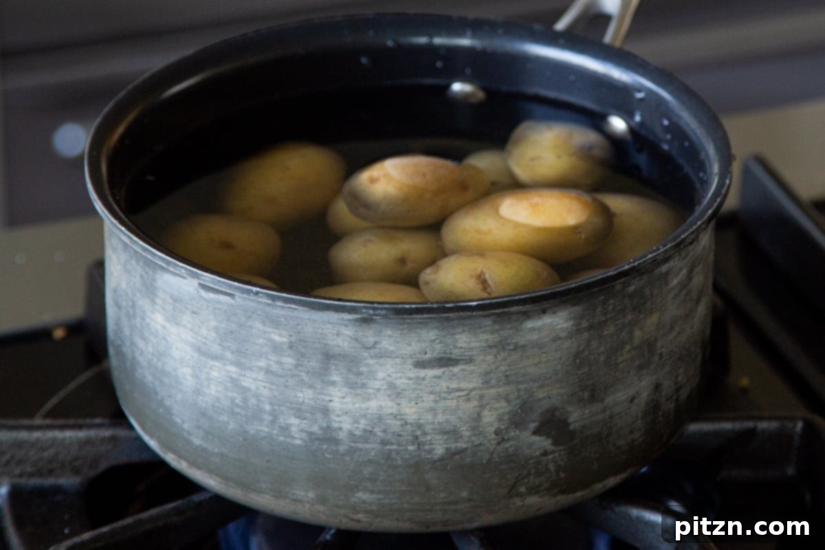 Potatoes simmering in a large pot on a stovetop, undergoing the initial cooking phase.