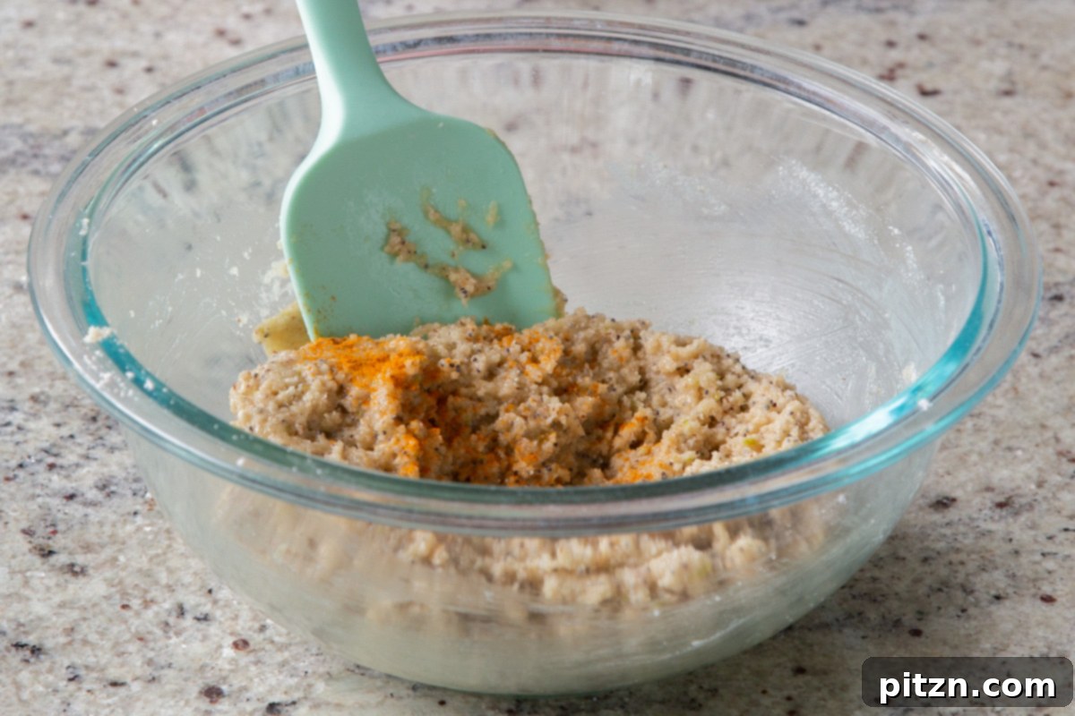 A beautifully vibrant yellow vegan lemon poppyseed cookie dough, freshly mixed with a pinch of turmeric for enhanced color, showcasing its smooth and soft consistency, ready for the next step.