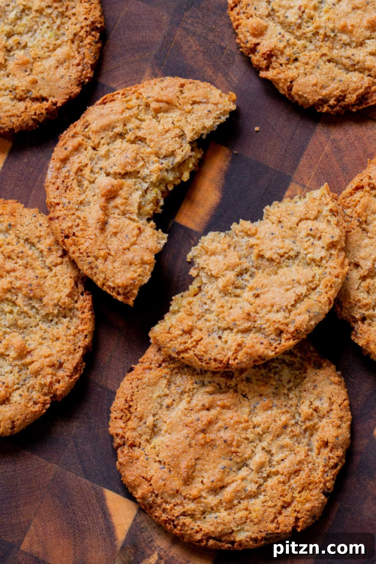 A perfectly baked vegan lemon poppyseed cookie, broken in half to reveal its soft, chewy interior and the delightful specks of poppyseeds, resting on a rustic wooden table.