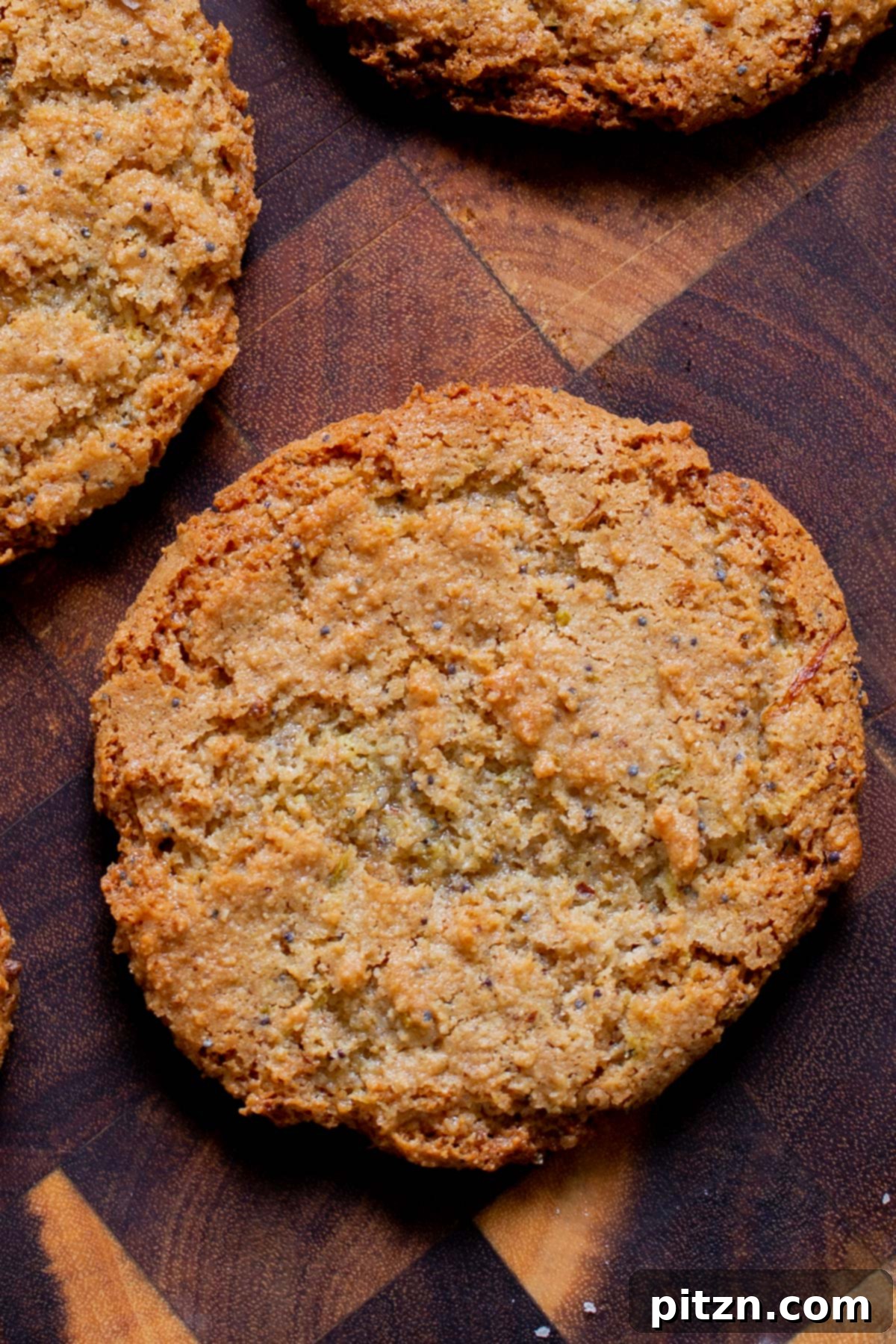 A close-up shot of a single golden-brown vegan lemon poppyseed cookie resting on a wooden surface, showcasing its vibrant zest and perfect texture.