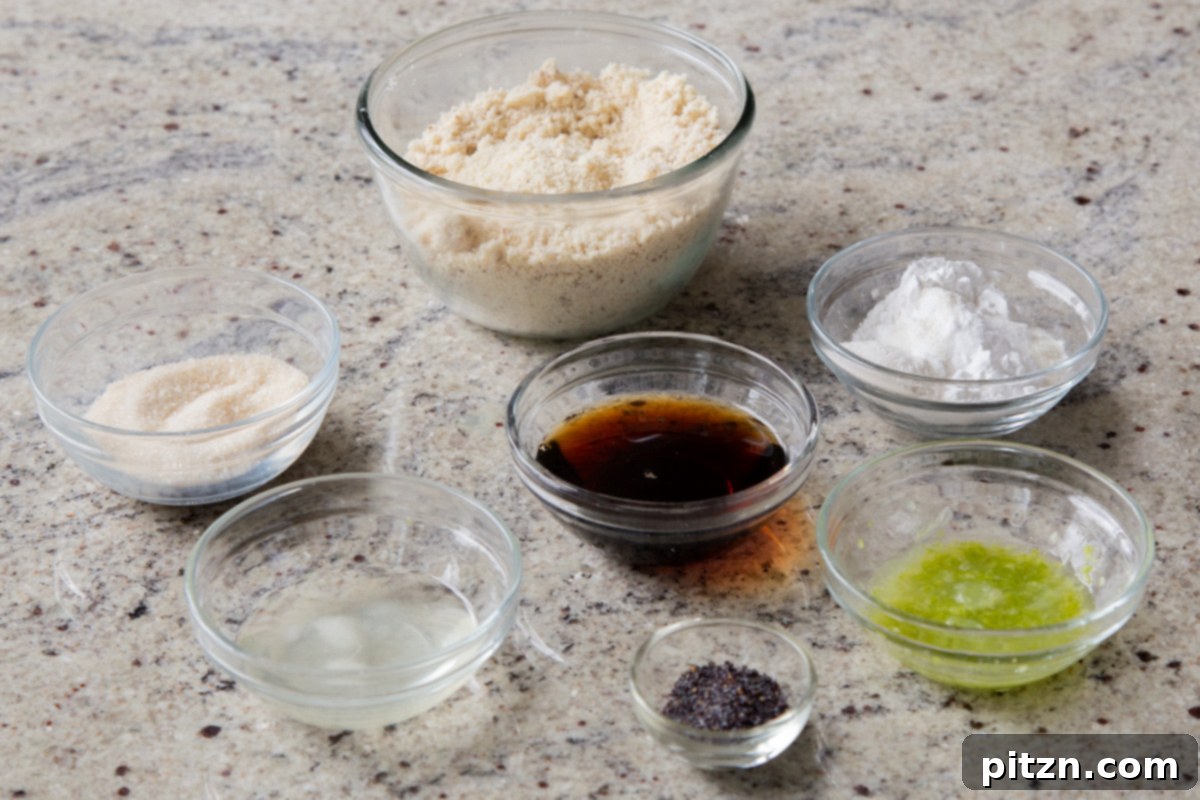 An array of fresh ingredients for vegan lemon poppyseed cookies, including vibrant lemon juice and zest, blanched almond flour, tapioca starch, and maple syrup, neatly presented in bowls on a kitchen countertop.