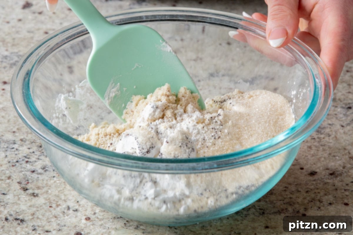 The initial stage of cookie preparation: a bowl containing all the dry ingredients – almond flour, tapioca starch, baking soda, salt, sugar, and poppyseeds – being thoroughly mixed together on a clean kitchen counter.