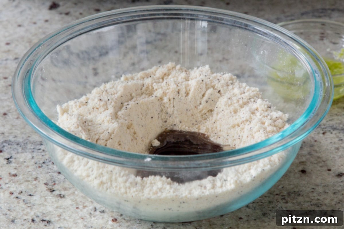 The precise moment wet ingredients, including melted coconut oil, maple syrup, lemon juice, zest, and vanilla, are carefully added to the created well in the dry cookie mix.