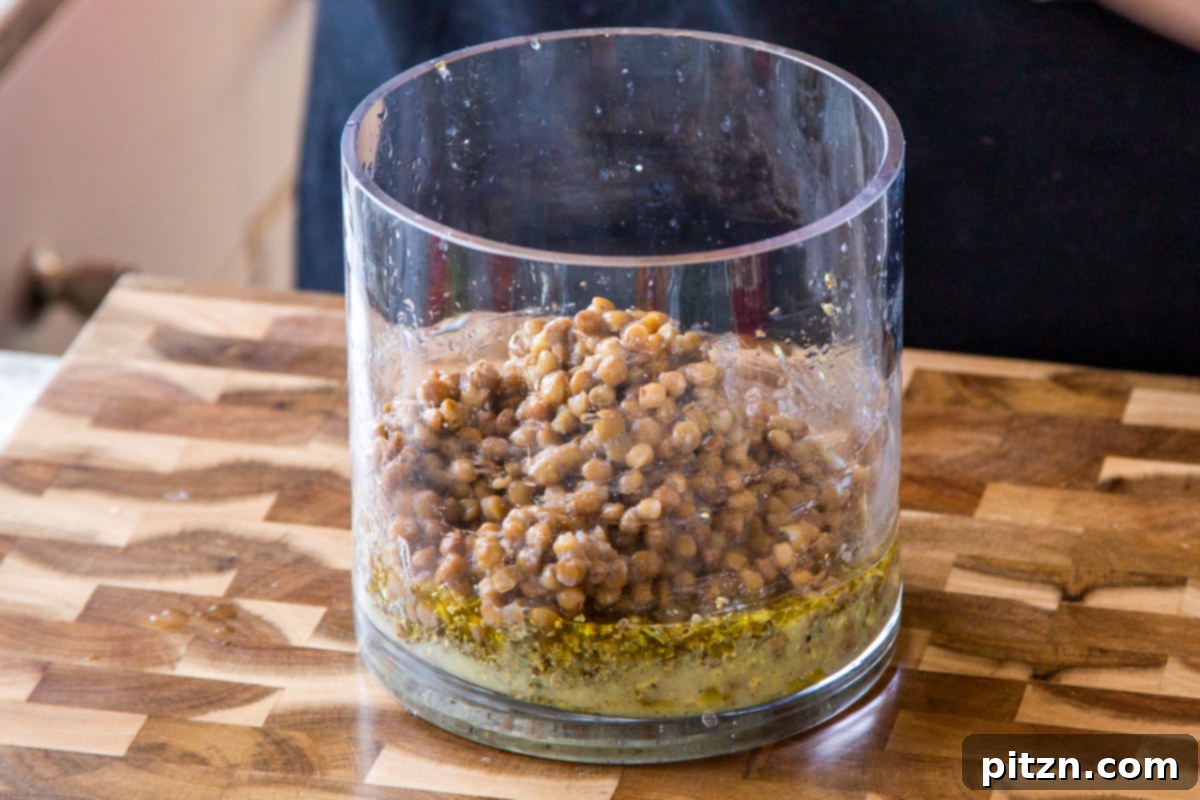 Effortless Lentil Quinoa Medley 14 The first layer of cooked lentils being gently spooned into the bottom of the glass jar, above the dressing.