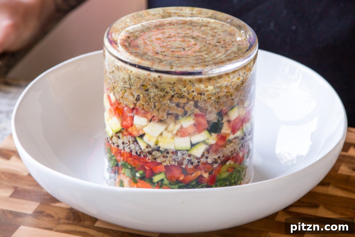Effortless Lentil Quinoa Medley 23 Inverting a glass jar of layered lentil quinoa salad into a large mixing bowl, ready to be tossed and served.