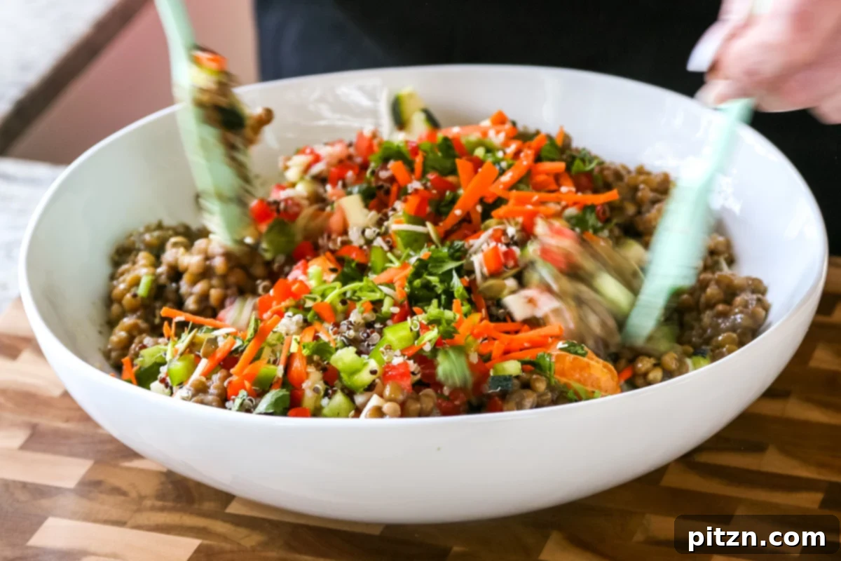 Effortless Lentil Quinoa Medley 25 Mixing the lentil quinoa salad with a serving spoon in a large bowl, ensuring the dressing evenly coats all the fresh ingredients.