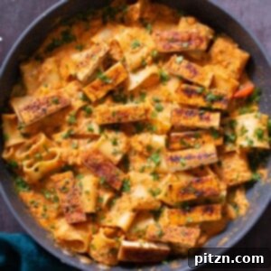 A vibrant skillet of romesco pasta, beautifully plated with spicy Cajun tofu on top.