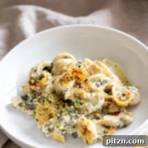 A generous serving of vegan spinach and artichoke pasta bake on a pristine white plate, ready to be enjoyed.